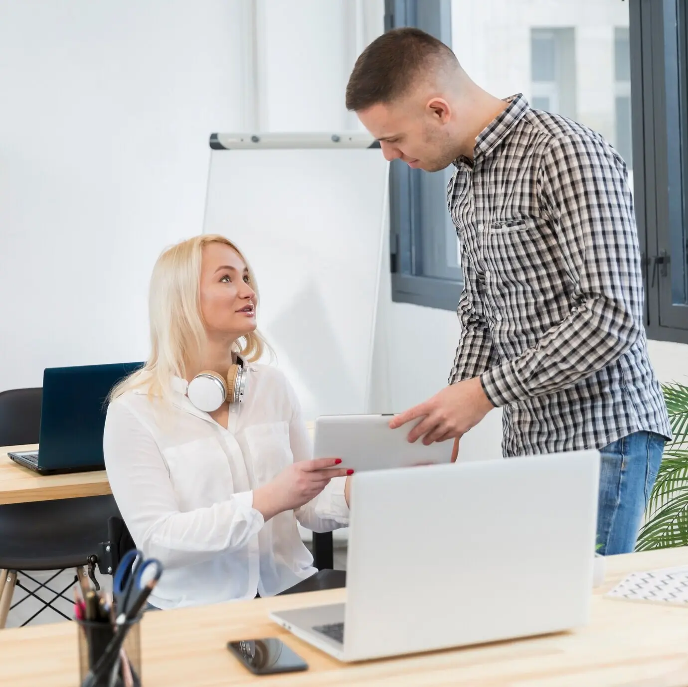 Seitenansicht einer Frau im Rollstuhl und einer Kollegin oder eines Kollegen, die/der ein Tablet hält.